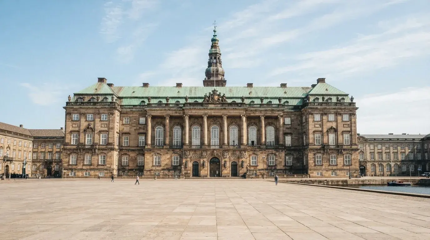 En historisk bygning i København med grøn kobbertag og kolonner i klart dagslys, set fra pladsen foran.